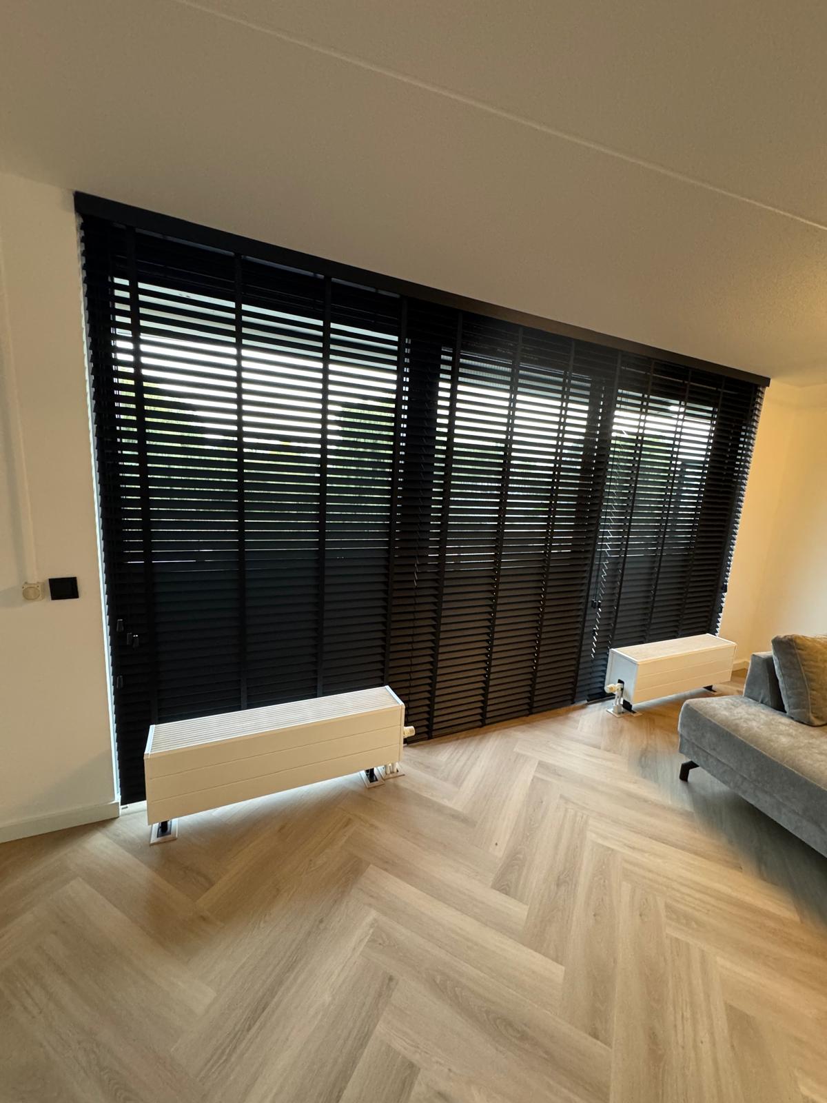 zwarte houten jaloezieën woonkamer inspiratie - Zwarte jaloezieën geven een strak en modern contrast in een lichte woonkamer.