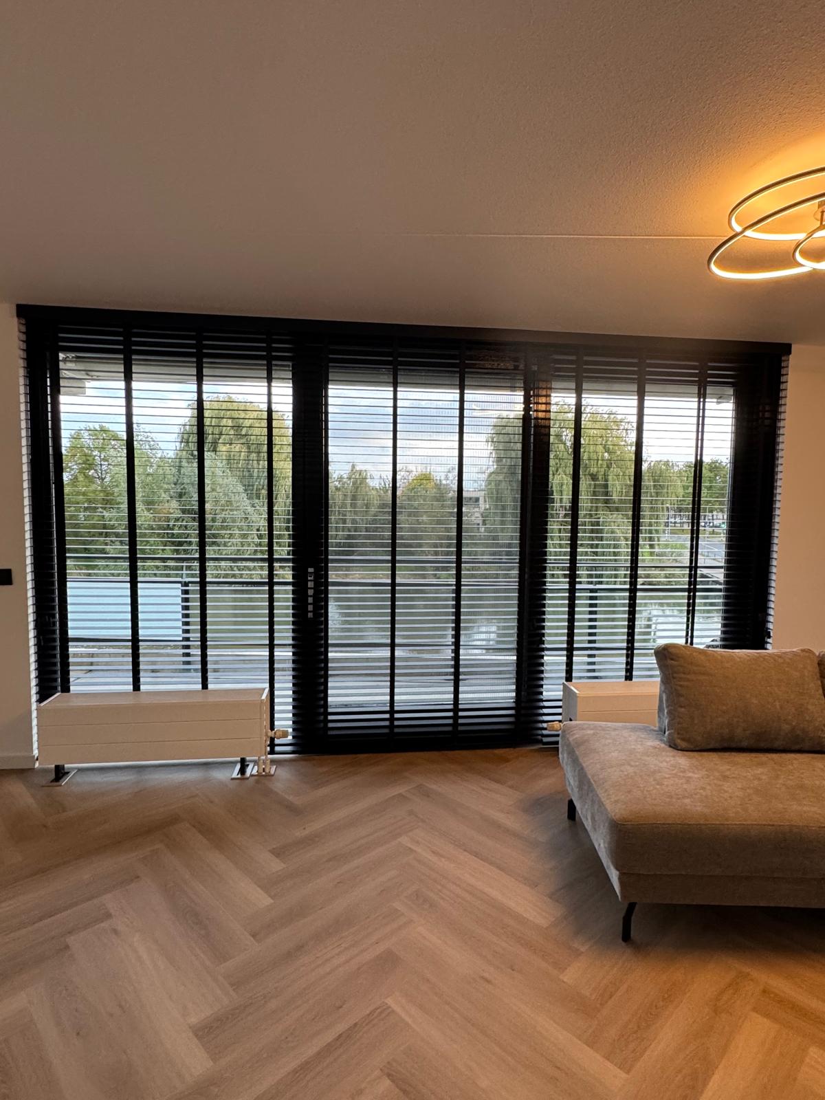 zwarte houten jaloezieën woonkamer inspiratie - Zwarte jaloezieën combineren prachtig met een warme houten visgraatvloer.