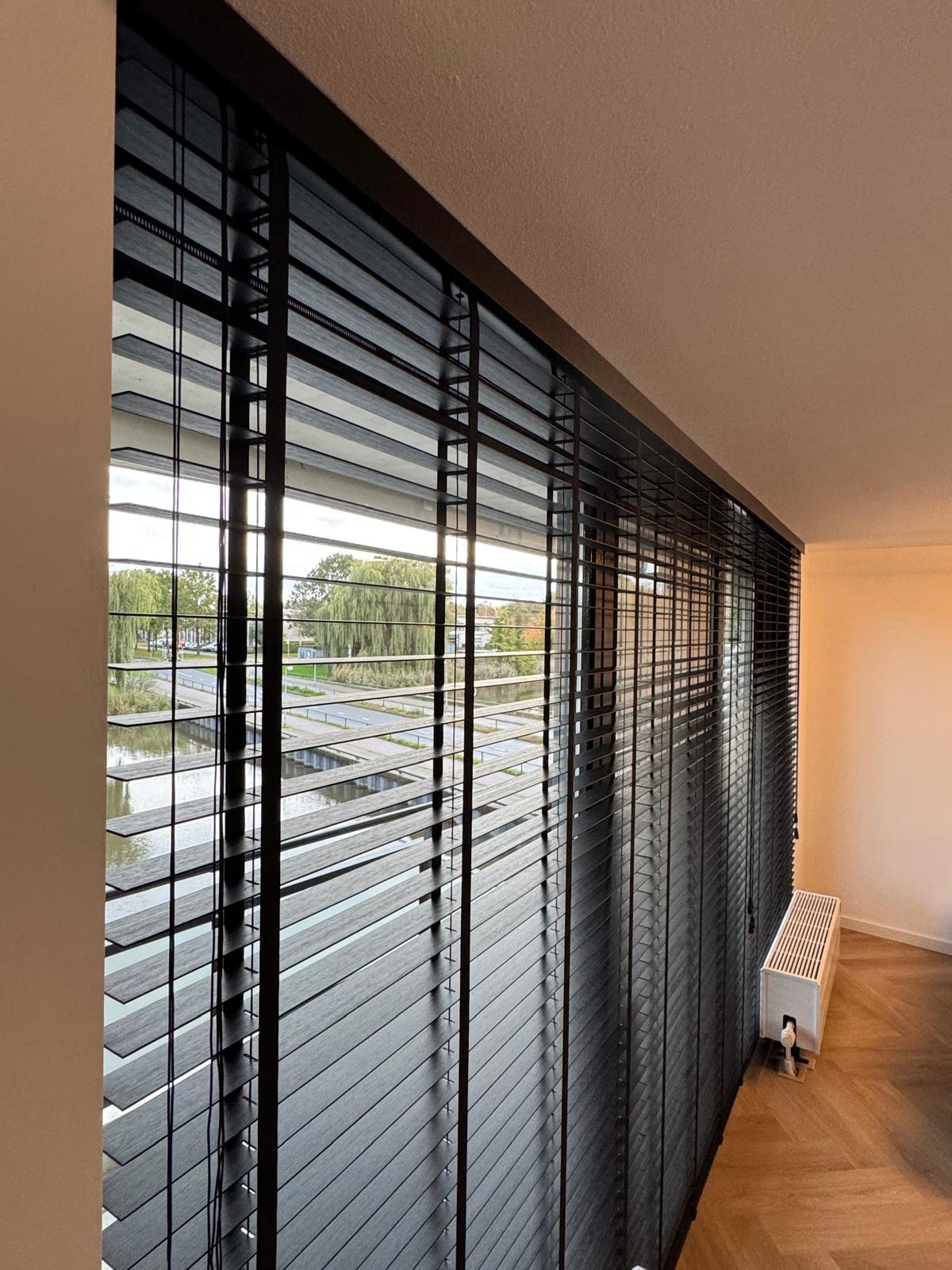 zwarte houten jaloezieën woonkamer - Zwarte houten jaloezieën voor een strakke look en sfeervolle lichtinval.