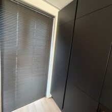 Antracietkleurige of zwarte aluminium jaloezieën in een modern interieur met een zwarte kastenwand en een lichte houten vloer.