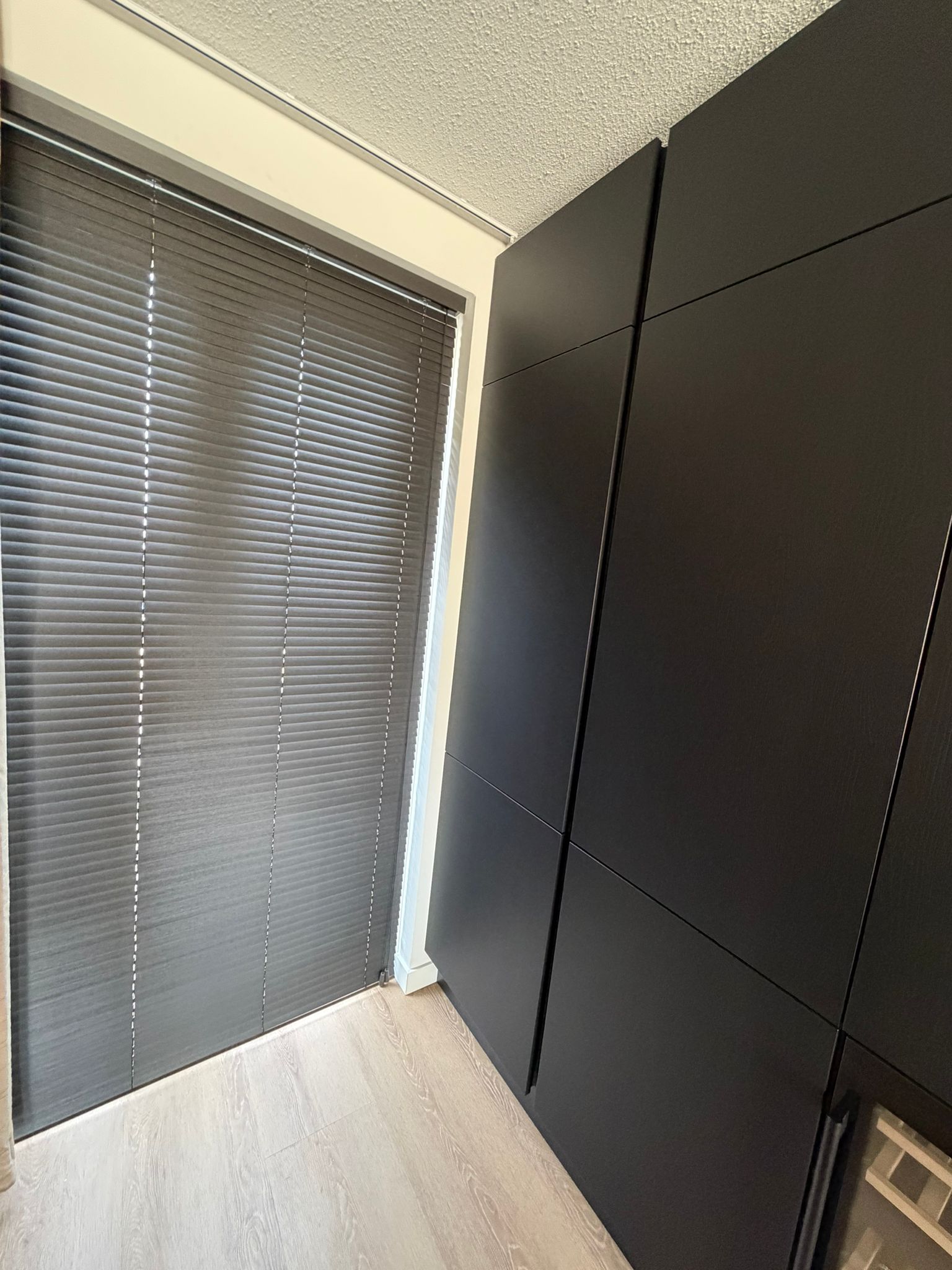 Een strak en modern geheel. Onze antraciet aluminium jaloezieën sluiten naadloos aan bij deze donkere kastenwand en creëren een rustige, stijlvolle sfeer.