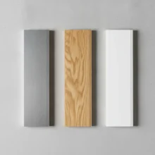 Drie stapels met stalen van jaloezie-lamellen in verschillende materialen naast elkaar: geborsteld aluminium, natuurlijk licht hout, en mat wit PVC.