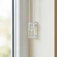 Close-up van een kettingspanner die de bedieningsketting van een rolgordijn strak tegen de muur houdt, als kindveilige oplossing.