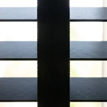 Detailopname van een houten jaloezie met brede ladderband die de gaatjes in de lamellen volledig bedekt en zo de lichtinval door de ponsgaten voorkomt.