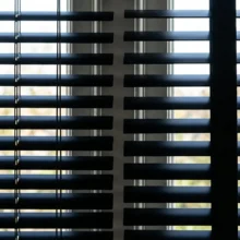 Detailfoto die het verschil toont tussen jaloezieën met een dun ladderkoord, waar licht door de gaatjes komt, en jaloezieën met een brede ladderband die de gaatjes afdekt.